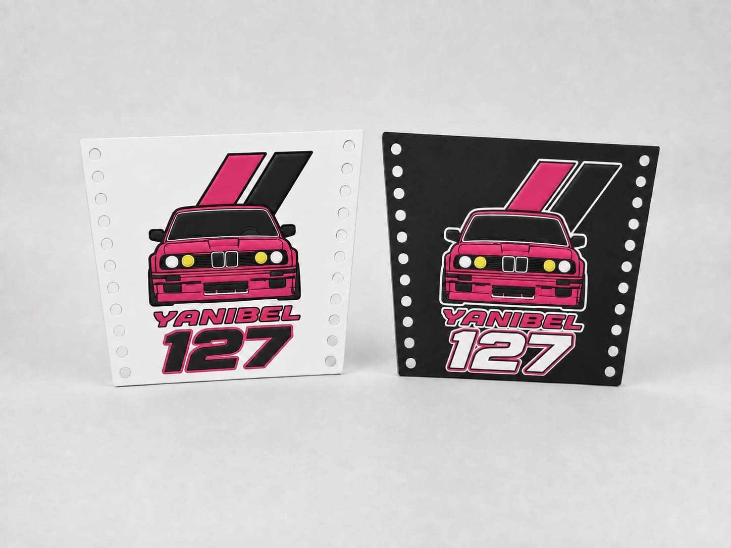 Dos fundas de mechero de silicona, una blanca y otra negra, con el frontal del BMW E30 rosa de faros amarillos y el texto YANIBEL 127